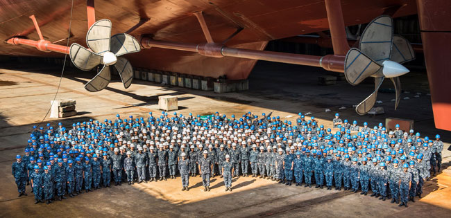 Shipbuilders take a photoop after completing the installation of the vessels' four propellers. All U.S. aircraft carriers procured since FY1958 have been built by Newport News Shipbuilding (NNS), of Newport News, VA, a shipyard that is part of Huntington Ingalls Industries (HII). NNS is the only U.S. shipyard that can build large-deck, nuclear-powered aircraft carriers. The aircraft carrier construction industrial base also includes hundreds of subcontractors and suppliers in various states. Photo: Huntington Ingalls Shipyards